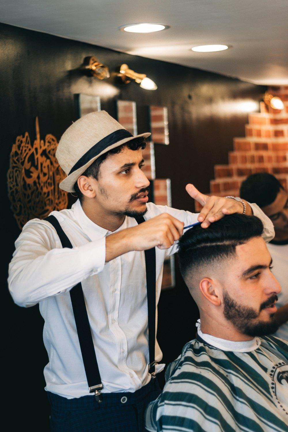 Barbier in Hut und Hosenträgern beim Stylen eines Herrenhaarschnitts